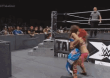 two women are wrestling in a wrestling ring with a referee in the background