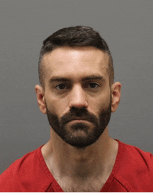 a man with a beard and a red shirt looks at the camera