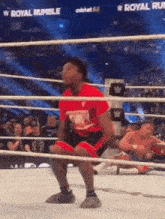 a wrestler in a red shirt is squatting in a wrestling ring .