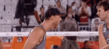 two men are playing volleyball on a court with a crowd in the background .