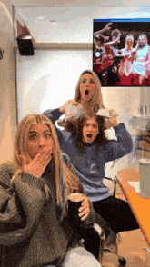 three girls are sitting in front of a television and one is holding a cup