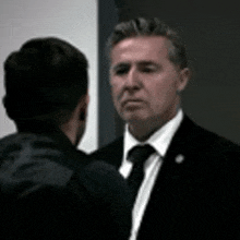 a man in a suit and tie is standing next to another man in a black jacket .