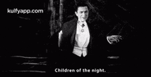 a black and white photo of a man in a tuxedo and bow tie standing in the dark .