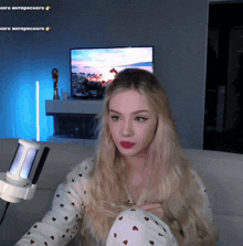 a woman sitting on a couch with a microphone in front of her and a tv in the background with russian writing on it