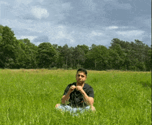a man in a black shirt sits in a lush green field