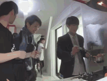 a man in a suit and tie is standing in a kitchen with other people .