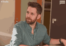 a man with a beard and a green shirt is sitting at a table .