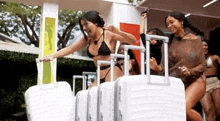 a woman in a bikini is holding a white suitcase .