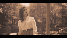 a woman wearing a white shirt and a brown skirt stands in a park