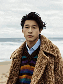 a young man wearing a striped sweater and a brown coat