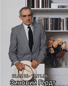 a man in a suit and tie stands in front of a bookshelf