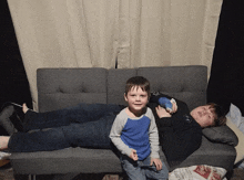 a boy is laying on a couch next to a little boy