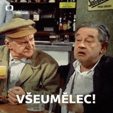 two men are sitting at a table with a sign that says " všeumelec " on it