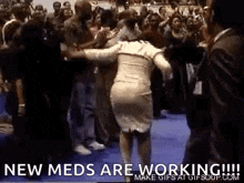 a woman is dancing in front of a crowd of people with the words `` new meds are working '' written on the bottom .
