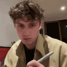 a young man with curly hair is holding a pen in his right hand