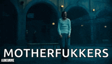 a man in a white shirt is standing in a dark room with the words `` motherfukkers '' written on the bottom .