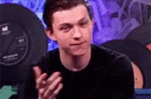 a man in a black shirt is clapping his hands in front of a speaker .
