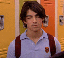 a young man wearing a blue polo shirt and a red backpack is standing in front of a row of school lockers .