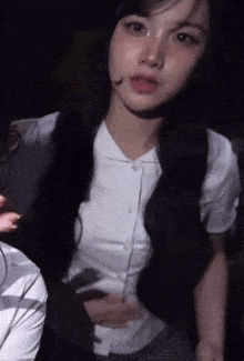 a woman with long black hair is wearing a white shirt and a microphone on her head .