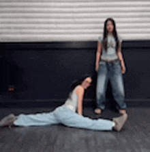 a woman is doing a split on the floor while another woman stands next to her .