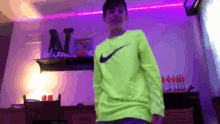 a boy wearing a neon green nike shirt is dancing in a room