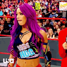 a woman with purple hair is standing in a wrestling ring with a crowd behind her .