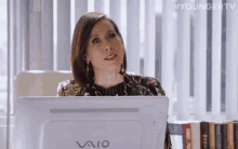 a woman is sitting at a desk in front of a vaio computer monitor .
