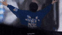 a man in a blue jacket is standing with his arms outstretched in front of a wall .