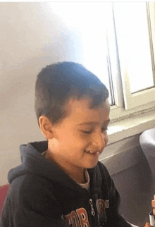 a young boy is sitting in front of a window with a marker in his hand .