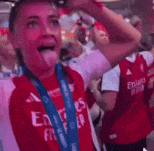 a woman wearing a red emirates jersey is holding a trophy in her hand