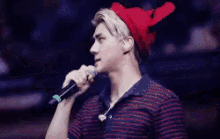 a young man is singing into a microphone while wearing a red hat .