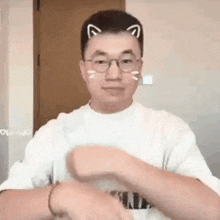 a man wearing glasses and a white shirt with cat ears on his head is making a funny face .