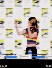 a woman in a rainbow top stands in front of a wall that says comic con on it