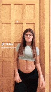 a woman wearing glasses is standing in front of a wooden door .