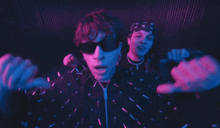 two men wearing sunglasses and a bandana are dancing in a dark room