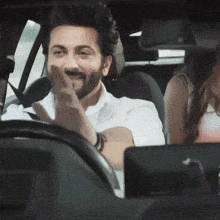 a man with a beard is sitting in the driver 's seat of a car with a woman in the back seat .