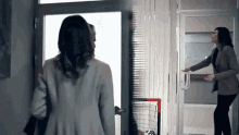 a woman is walking through a doorway while another woman is standing in front of a goal .