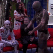 a man in a mummy costume is dancing in front of a group of people sitting on a red couch .