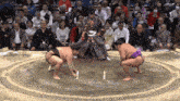 two sumo wrestlers are squatting down in a ring with a referee in the background