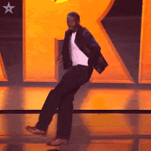 a man in a white shirt and black jacket is dancing on a stage in front of the letter r