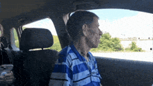 a man in a blue and white striped shirt is sitting in the driver 's seat of a car