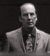 a man in a suit and tie is standing in a dark room and looking at the camera .