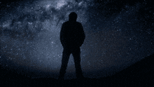 a silhouette of a man stands in front of a starry sky