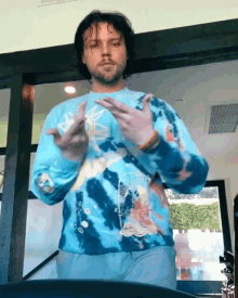 a man wearing a blue tie dye sweater is making a peace sign