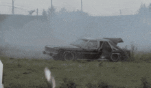 a man stands in front of a destroyed car in a field