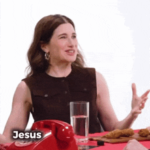 a woman is sitting at a table with a red telephone , a glass of water , and chicken nuggets .
