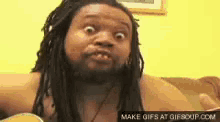 a man with dreadlocks and a beard is sitting on a couch making a funny face .