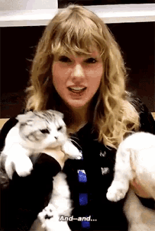 a blonde woman is holding two cats and says " and-and "