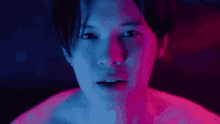 a close up of a man 's face in a dark room with blue and pink lights behind him .