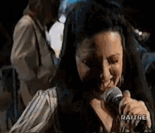 a woman is singing into a microphone on a stage in a dark room .